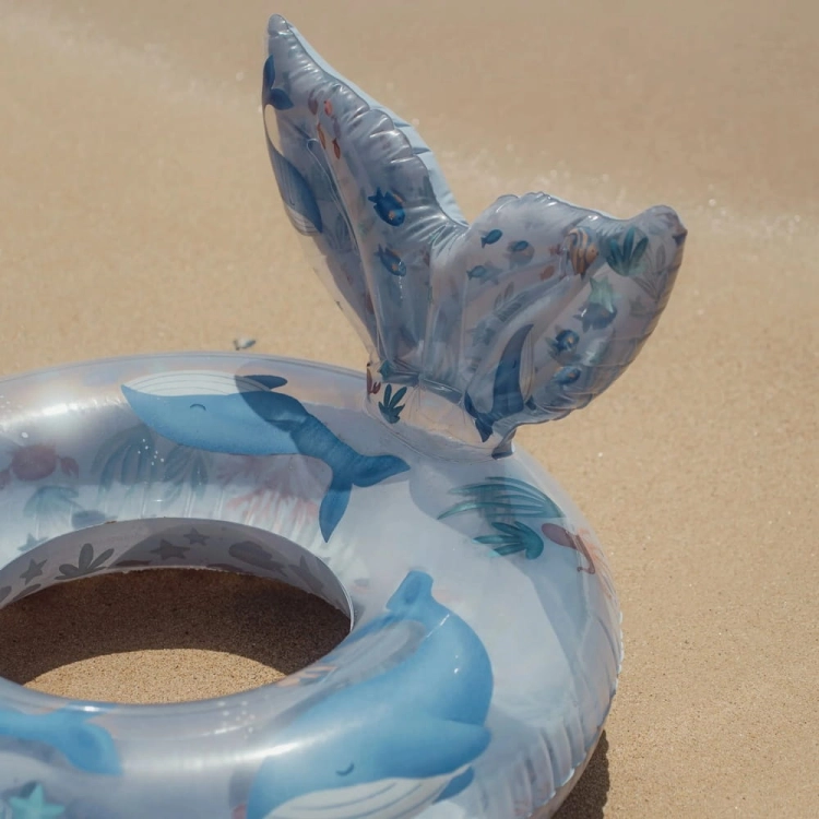 Koło do pływania Ocean World 91cm Little Dutch na piasku – zbliżenie na ogon wieloryba i nadruk zwierząt morskich