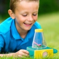 Chłopiec bawiący się mikroskopem Itty-Bitty Microscope B.toys w ogrodzie – obserwacja owadów przez lupę, zabawka edukacyjna na świeżym powietrzu