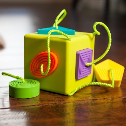 Sorter Kostka OombeeCube Fat Brain Toys – zielona sensoryczna kostka z kształtami koło, kwadrat i pięciokąt na sznurkach, zabawka dla niemowląt