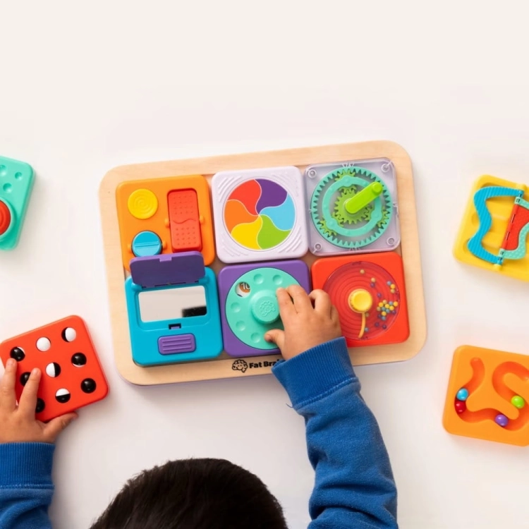 Tablica PlayTab Fat Brain Toys – widok z góry na zestaw wszystkich paneli aktywności wokół drewnianej tablicy, dziecko eksploruje różne faktury i mechanizmy, kompletny zestaw sensoryczny dla niemowląt i małych dzieci