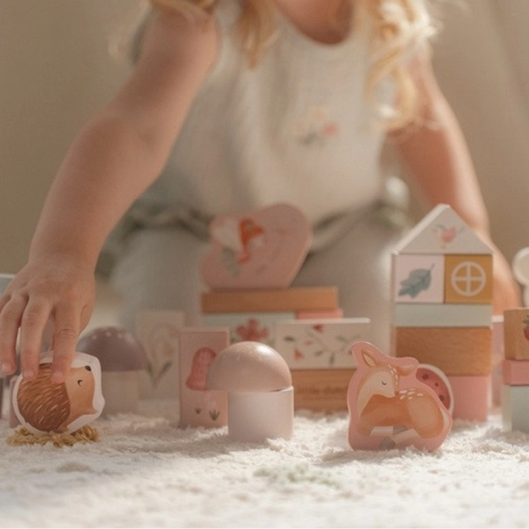 Zestaw klocków Fairy Garden FSC Little Dutch – dziewczynka bawi się różowymi drewnianymi klockami z motywem wróżek, jeżykiem i jelonkiem na białym dywanie