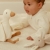 Zestaw prezentowy Dzianinowy Newborn Naturals Little Dutch – zbliżenie na dzianinową gęś i małą przytulankę królika obok leżącego niemowlęcia na białej powierzchni