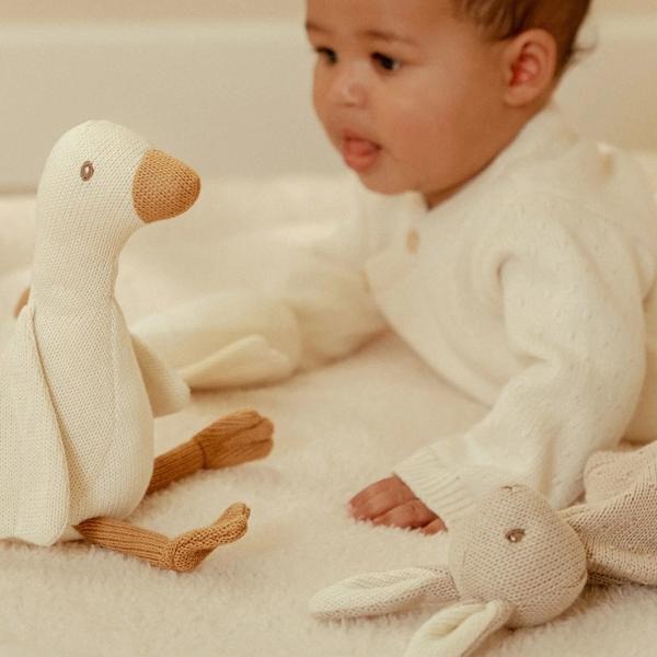 Zestaw prezentowy Dzianinowy Newborn Naturals Little Dutch – zbliżenie na dzianinową gęś i małą przytulankę królika obok leżącego niemowlęcia na białej powierzchni