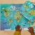 Dziecko układa ostatnie elementy puzzli Mapa świata Janod przy walizce na drewnianym blacie