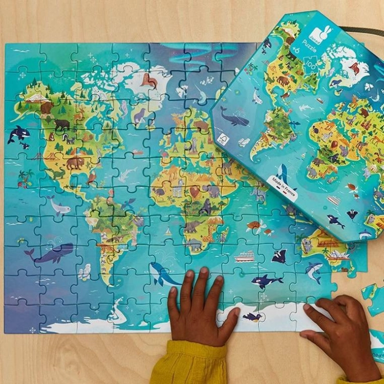 Dziecko układa ostatnie elementy puzzli Mapa świata Janod przy walizce na drewnianym blacie