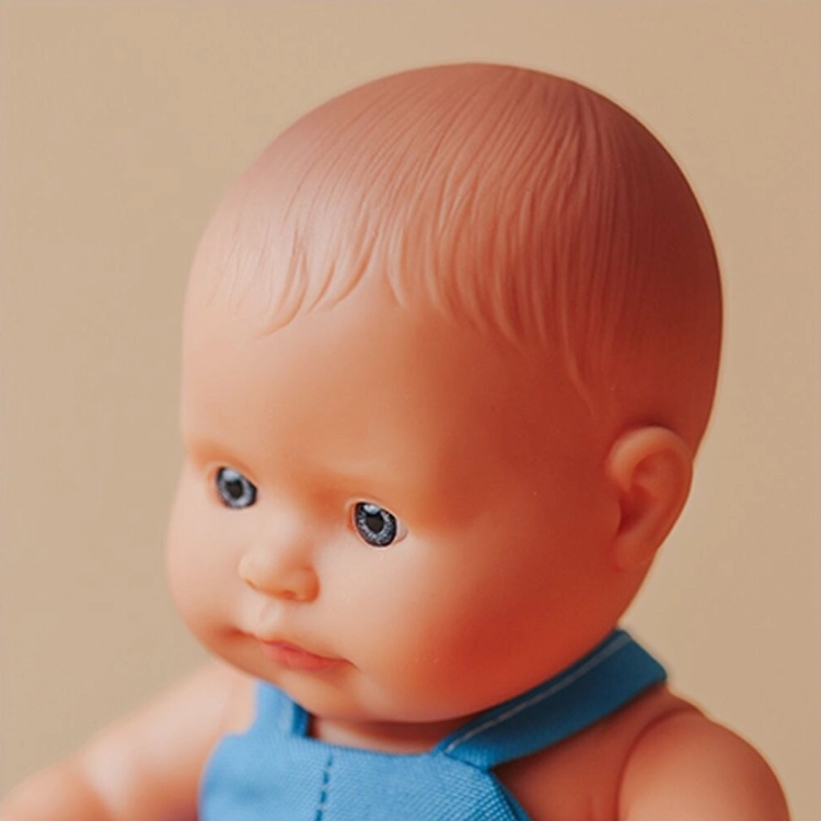 Zbliżenie na twarz lalki Miniland Baby 21 cm: niebieskie oczy i włosy wyrzeźbione w materiale lalki