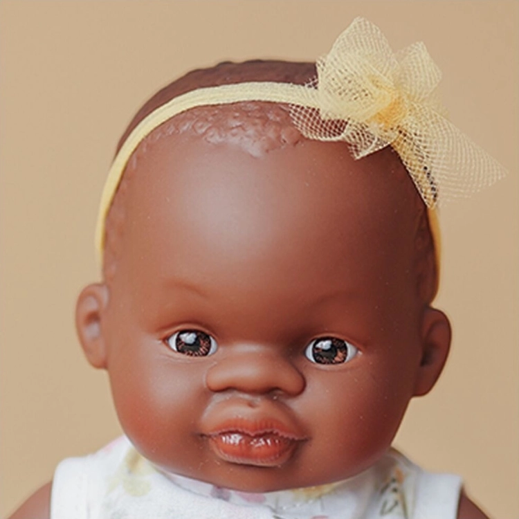 Zbliżenie na twarz lalki dziewczynki Miniland Baby 21 cm z brązowymi oczami i żółtą opaską z tiulową kokardką