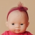 Zbliżenie na twarz lalki dziewczynki Miniland Baby 21 cm z ciemnymi oczami i bordową opaską z tiulową kokardką