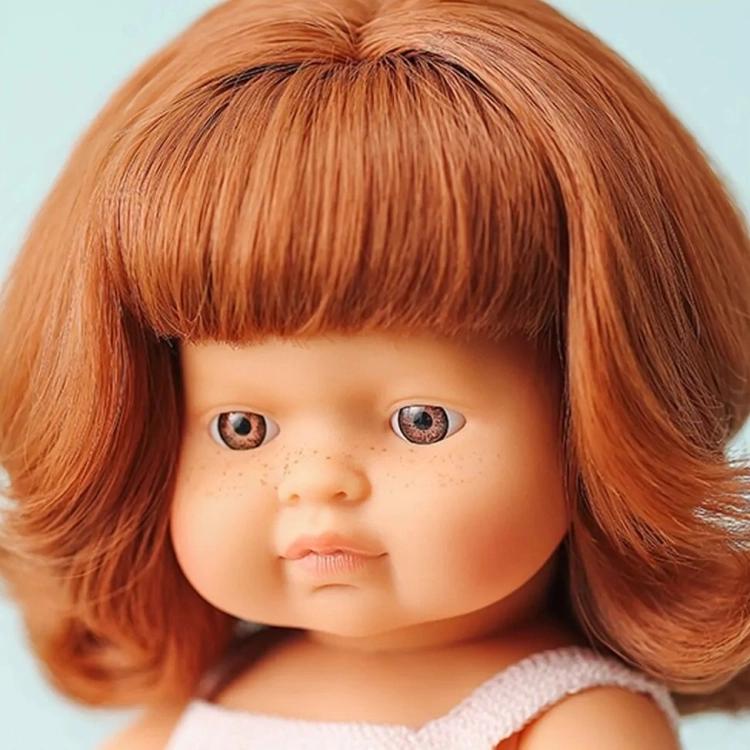 Zbliżenie na twarz lalki Miniland 38 cm: rude włosy z grzywką, brązowe oczy i piegi na policzkach