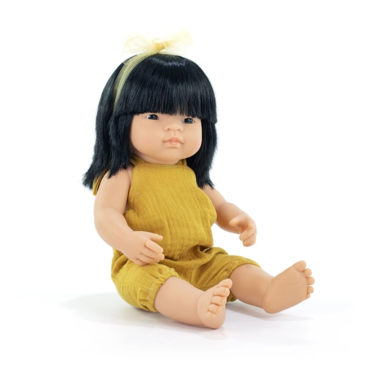 Lalka dziewczynka Miniland My Friends & Me 38 cm z czarnymi włosami i grzywką, w musztardowym kombinezonie, na białym tle