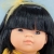 Zbliżenie na twarz lalki dziewczynki Miniland 38 cm: proste czarne włosy z grzywką, ciemne oczy i żółta opaska z tiulu