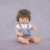 Lalka chłopiec Miniland 38 cm z brązowymi włosami, w białej koszulce i ogrodniczkach w serduszka, siedząca na lawendowym tle