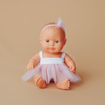 Mała lalka dziewczynka Miniland 21 cm w białej sukience z tiulową spódniczką, siedząca na beżowym tle